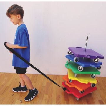 A child pulling a stack of rainbow-colored scooter boards using a black pull strap attached to the top scooter.