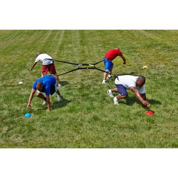 Four adult players secured in a 4-way harness. Each player is pulling in a different direction, attempting to grab a ball off of a cone.