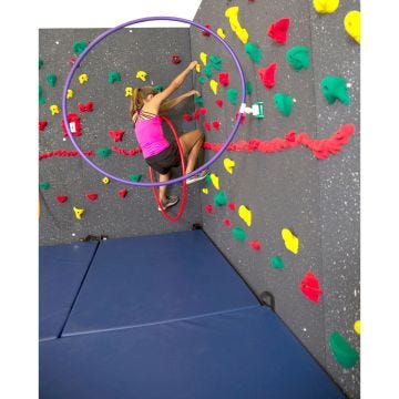 A female student traversing a climbing wall. The wall is affixed with many hand holds, including one securing a plastic hoop.