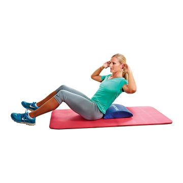 An adult female leaning back on a blue abdominal cushion, on a red workout mat.