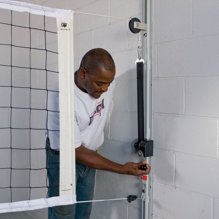 Man adjusting wall mounted volleyball system net infinitely adjusted from 42" (tennis) to 96" (men's volleyball) net height. Man adjusting wall mounted volleyball system net infinitely adjusted from 42" (tennis) to 96" (men's volleyball) net height.
