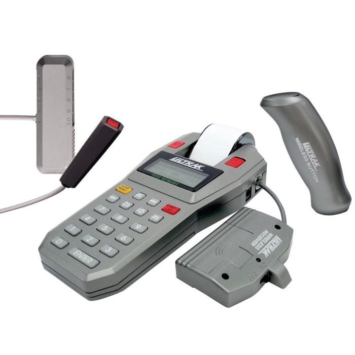 A close-up view of a timer system featuring a handheld digital timer, a wireless button, and accompanying hardware in gray and black A close-up view of a timer system featuring a handheld digital timer, a wireless button, and accompanying hardware in gray and black